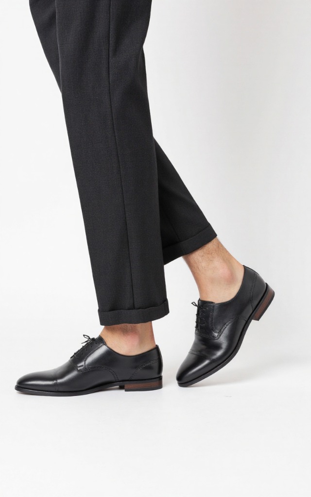 A male model wearing Oxford shoes, against a white background, with a close   up of the feet